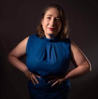 femme en tee shirt bleu et jupe en jeen avec les mains qui encadrent les hanches