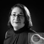 Portrait Corporate 16/9ème en noir et blanc pour projet numérique et impression photographie corporate en noir et blanc de femme au tee-shirt col américain et avec des lunettes