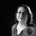 Portrait Corporate 16/9ème en noir et blanc pour projet numérique et impression photographie corporate en noir et blanc de femme au tee-shirt rouge et avec des lunettes