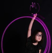Petite fille en robe noir dessinant un cercle de lumière autour d'elle et dessinant une main