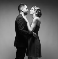 Photo d'hmme et femme noir et blanc de plein pieds, enlacés l'un contre l'autre. L'homme est en costume foncé et la femme en petite robe.